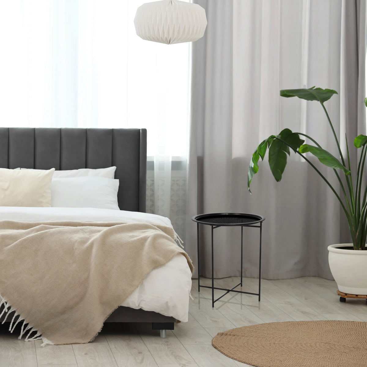 Tavolino ALLRUND nero in metallo con piano traforato accanto a un letto di hjh LIVING