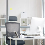 Sedia da ufficio professionale CAPTIVO BASE W grigia con schienale in rete e poggiatesta a una scrivania di hjh OFFICE