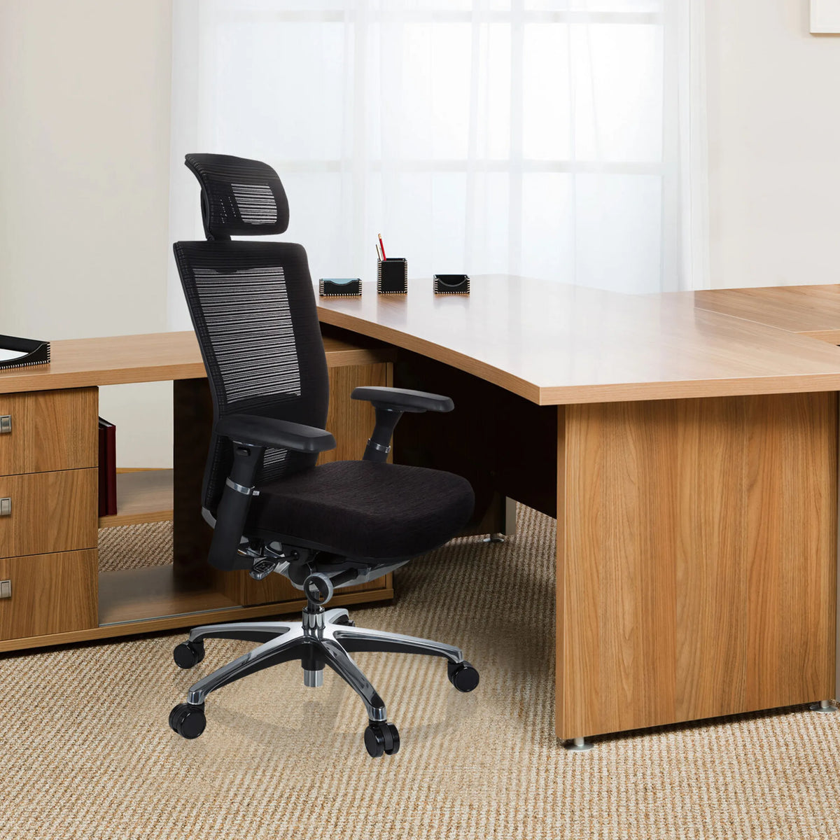 High-end Sedia da ufficio NOVA PRO I nera con schienale in rete e poggiatesta davanti a una scrivania di hjh OFFICE
