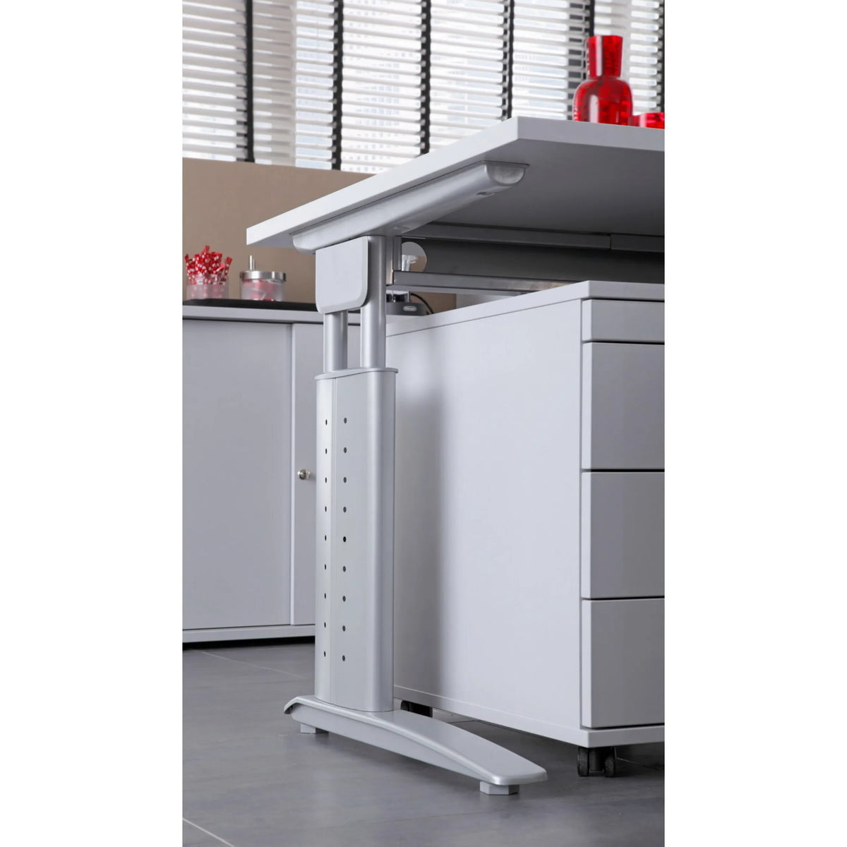 Struttura regolabile in altezza argento della scrivania UNDA 18 S accanto a un cassettiera grigia su ruote di hjh OFFICE PRO