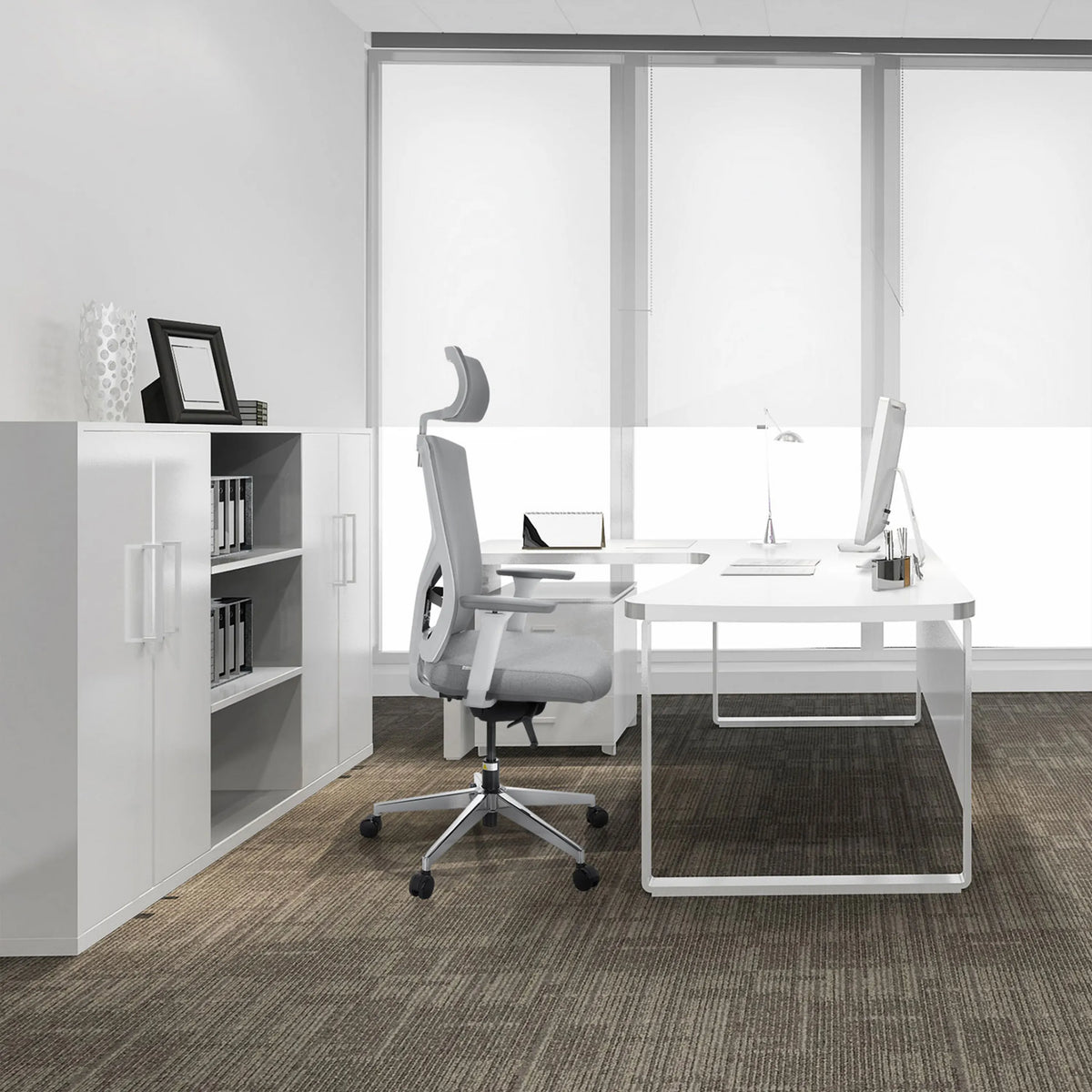 Sedia da ufficio professionale BRETON PRO W grigia con poggiatesta e braccioli davanti a una scrivania bianca di hjh OFFICE