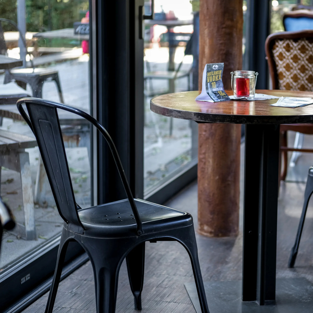Sedia bistro nera VANTAGGIO BRUSH con schienale curvo a un tavolo rotondo di hjh OFFICE