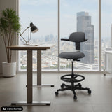 Sedia da lavoro TOP WORK 40 grigio scuro con poggiapiedi e rotelle davanti a una finestra di hjh OFFICE (immagine generata dall’IA)