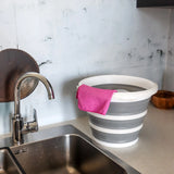 Contenitore pieghevole CLEAN SILR grigio e bianco con un panno rosa su una superficie di lavoro accanto a un lavandino di hjh OFFICE