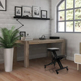 Sgabello per ginocchia ORTHONI nero con ruote davanti a una scrivania in legno in una stanza luminosa di hjh OFFICE
