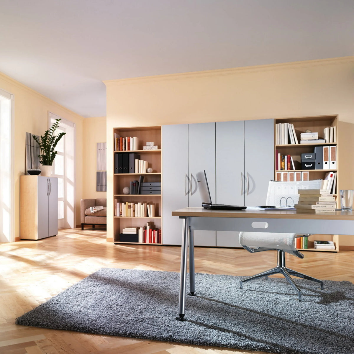 Scrivania regolabile in altezza ATOS 18 S in rovere rustico con laptop e sedia da ufficio in una stanza luminosa di hjh OFFICE PRO