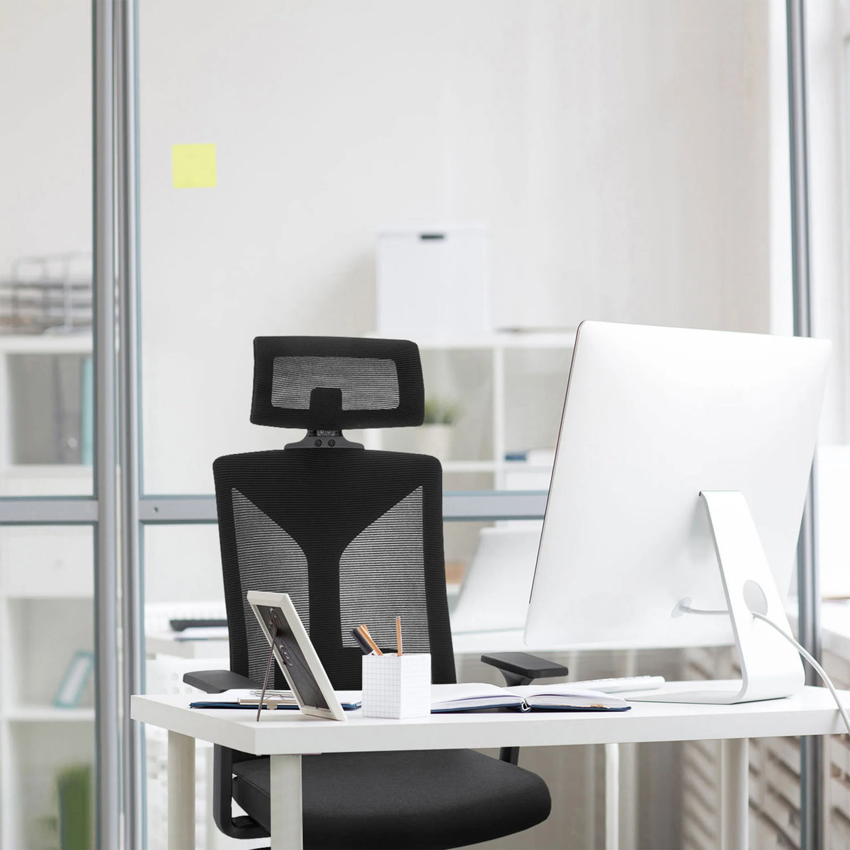 Sedia da ufficio professionale KODIAK nera con schienale in rete e poggiatesta a una scrivania bianca di hjh OFFICE