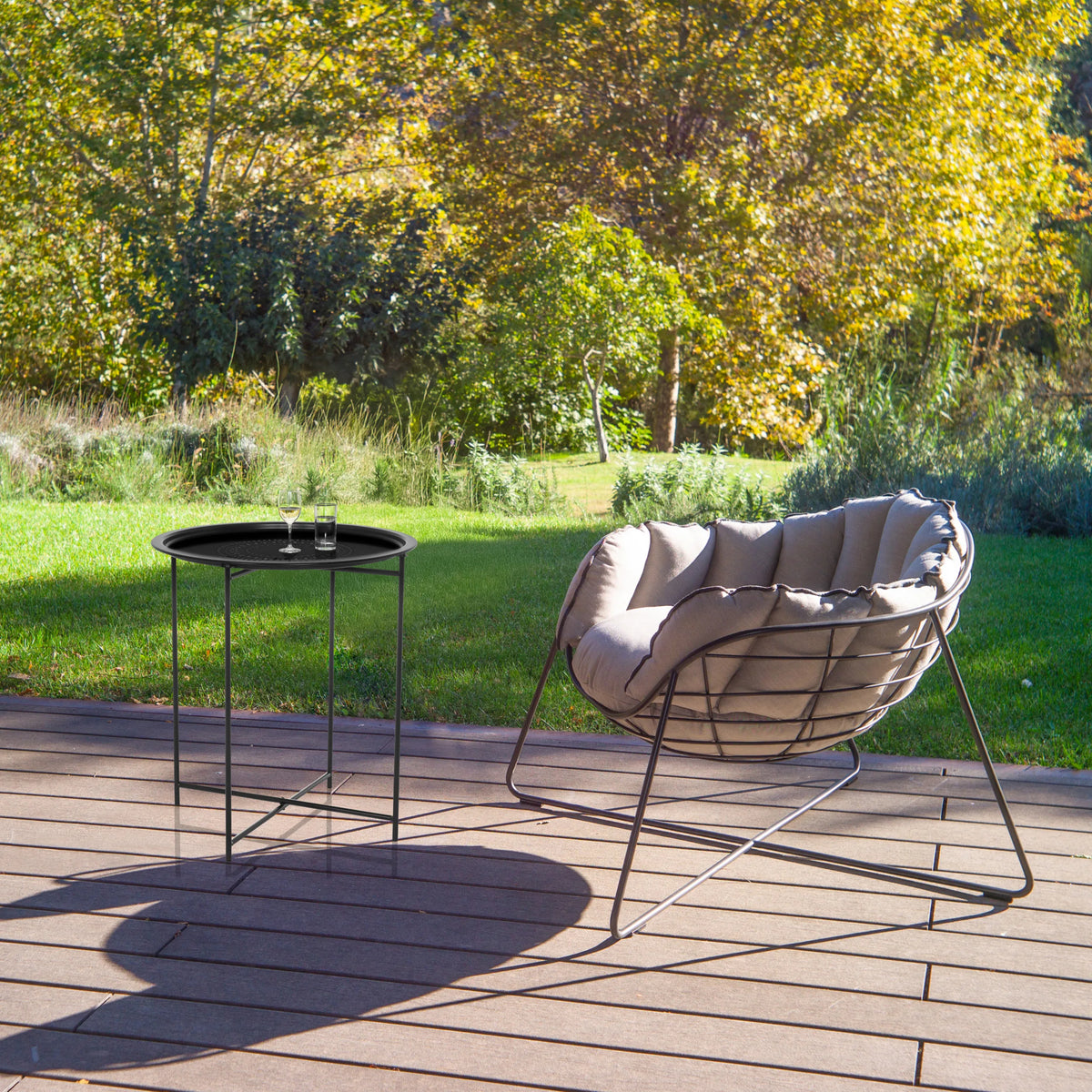 Tavolino ALLRUND in metallo nero con motivo traforato su una terrazza accanto a una poltrona lounge di hjh LIVING