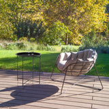Tavolino ALLRUND in metallo nero con motivo traforato su una terrazza accanto a una poltrona lounge di hjh LIVING